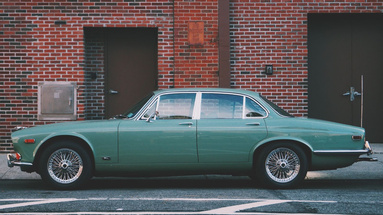 Green classic four-door sedan with wire wheels parked along a brick building